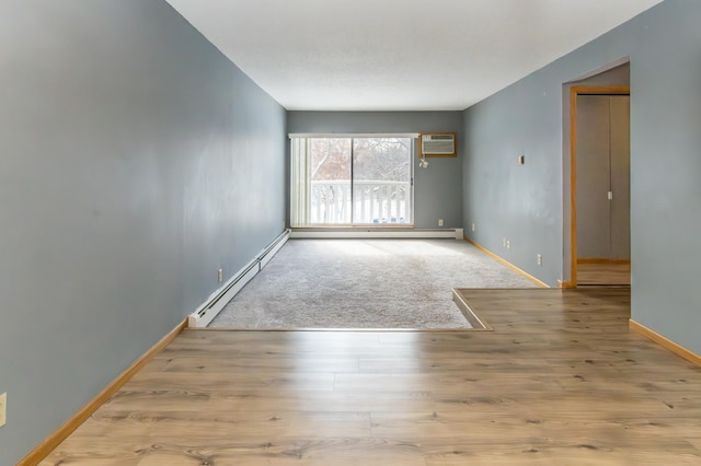 unfurnished room featuring a baseboard radiator, an AC wall unit, baseboards, and wood finished floors