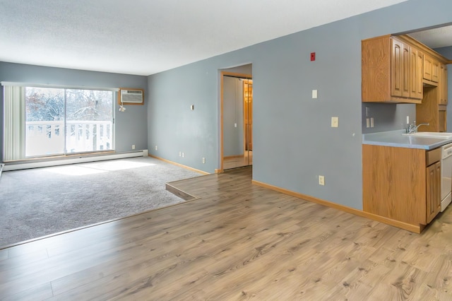 interior space with baseboard heating, light wood-style floors, a sink, dishwasher, and baseboards