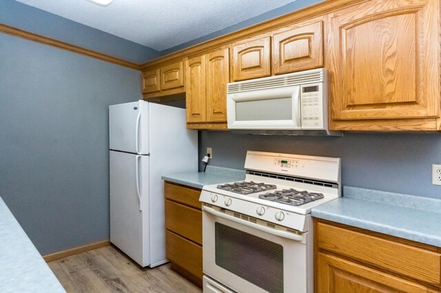 kitchen with white appliances, baseboards, light countertops, and light wood-style floors