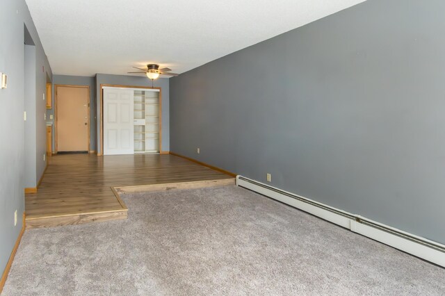 spare room featuring baseboard heating, a ceiling fan, carpet flooring, wood finished floors, and baseboards