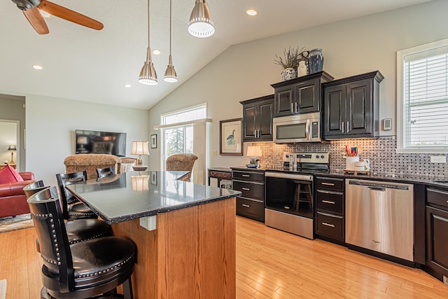 kitchen with appliances with stainless steel finishes, hanging light fixtures, a kitchen breakfast bar, a center island, and light hardwood / wood-style floors