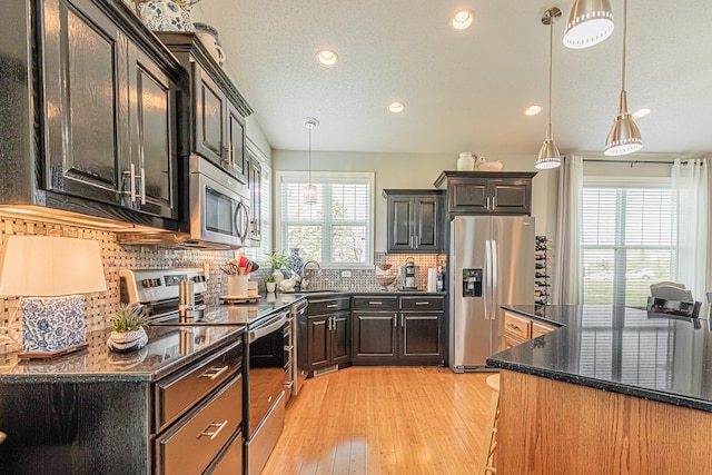 kitchen with hanging light fixtures, appliances with stainless steel finishes, sink, and dark stone counters