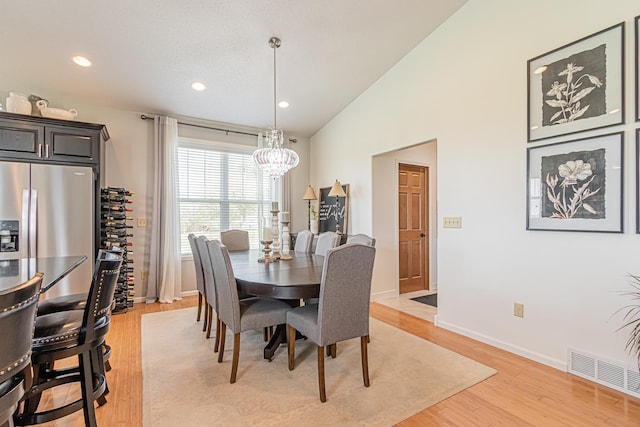 dining space with lofted ceiling, a chandelier, and light hardwood / wood-style flooring