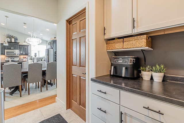 kitchen featuring appliances with stainless steel finishes, white cabinetry, hanging light fixtures, light tile patterned floors, and a notable chandelier