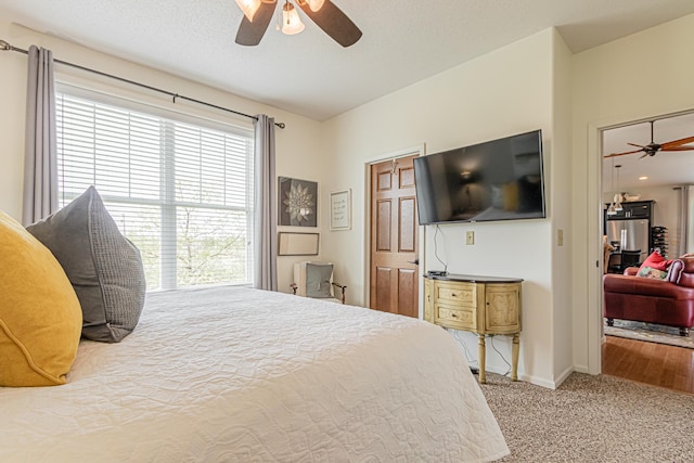 carpeted bedroom featuring a textured ceiling, ceiling fan, and stainless steel fridge with ice dispenser