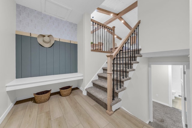 stairs with beam ceiling, hardwood / wood-style flooring, and a high ceiling