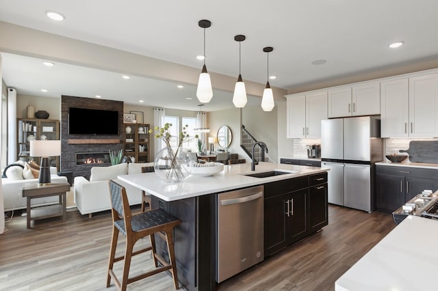 kitchen featuring sink, decorative light fixtures, stainless steel appliances, a kitchen island with sink, and white cabinets