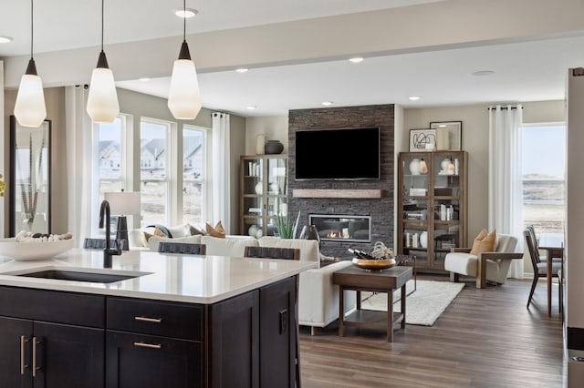 kitchen with an island with sink, a stone fireplace, sink, and decorative light fixtures