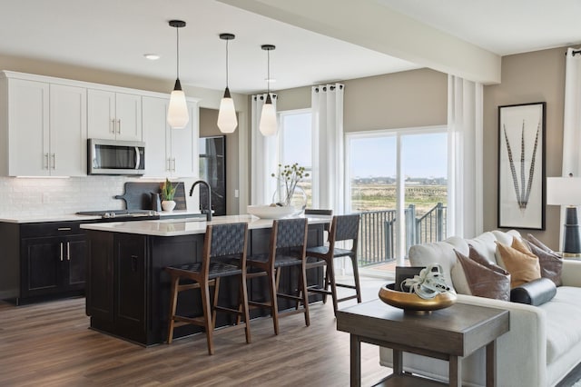 kitchen featuring white cabinetry, hanging light fixtures, a kitchen breakfast bar, an island with sink, and backsplash