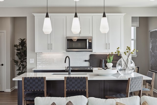 kitchen featuring white cabinetry, backsplash, decorative light fixtures, and an island with sink