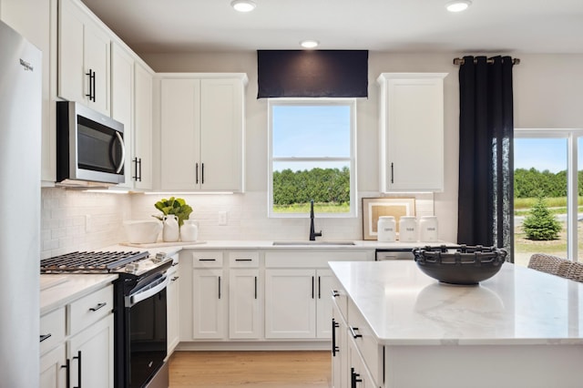 kitchen with range with gas cooktop, white cabinetry, sink, decorative backsplash, and light stone counters