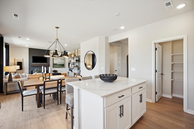 kitchen featuring white cabinetry, a center island, light hardwood / wood-style floors, and light stone counters