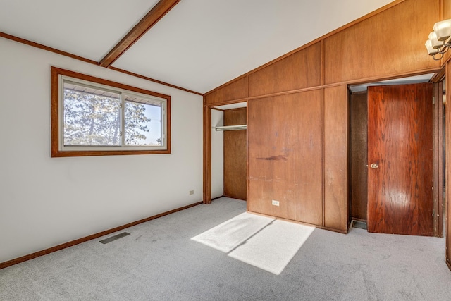 unfurnished bedroom with crown molding, a closet, lofted ceiling, and light carpet