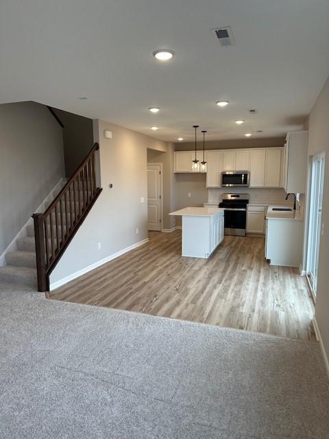 kitchen featuring white cabinetry, a center island, hanging light fixtures, light hardwood / wood-style flooring, and appliances with stainless steel finishes