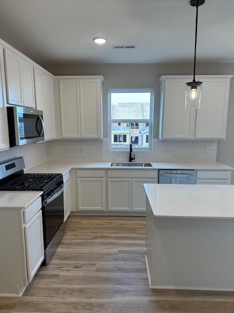 kitchen featuring sink, appliances with stainless steel finishes, hanging light fixtures, tasteful backsplash, and white cabinets