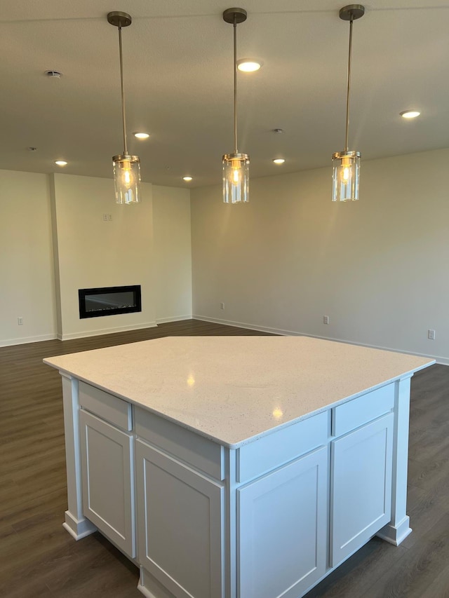 kitchen with white cabinetry, hanging light fixtures, light stone counters, and dark wood-type flooring