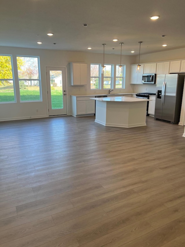 kitchen with stainless steel appliances, pendant lighting, white cabinets, and light hardwood / wood-style flooring