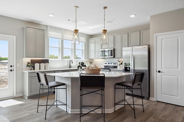 kitchen featuring a breakfast bar, wood-type flooring, hanging light fixtures, appliances with stainless steel finishes, and a kitchen island