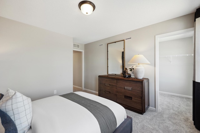 bedroom with a walk in closet, light colored carpet, and a closet