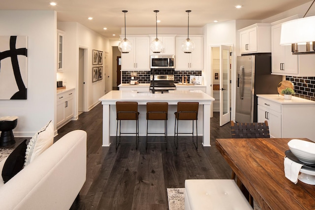 kitchen with a center island with sink, appliances with stainless steel finishes, dark hardwood / wood-style flooring, pendant lighting, and white cabinets