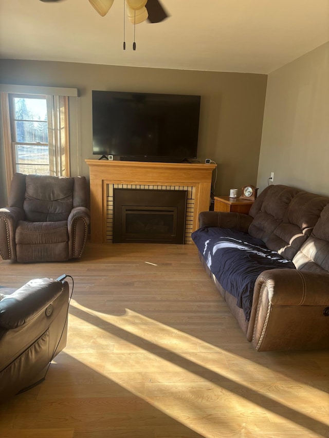 living room with a brick fireplace, light hardwood / wood-style floors, and ceiling fan