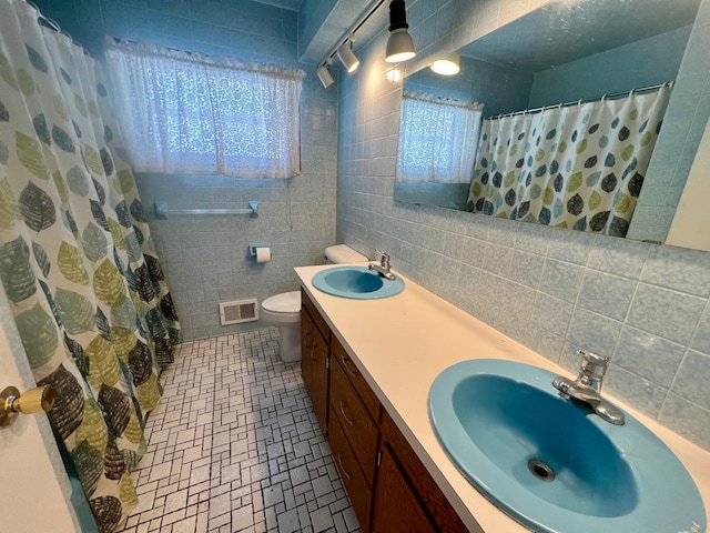 bathroom featuring walk in shower, vanity, toilet, and tile walls