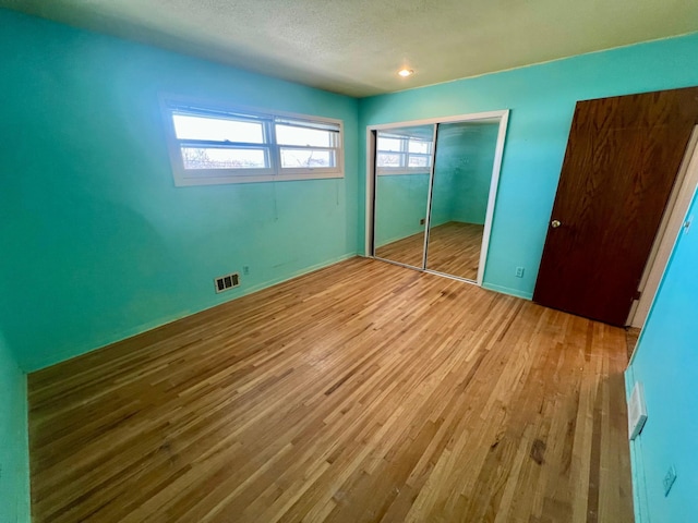 unfurnished bedroom featuring a textured ceiling, a closet, and light wood-type flooring