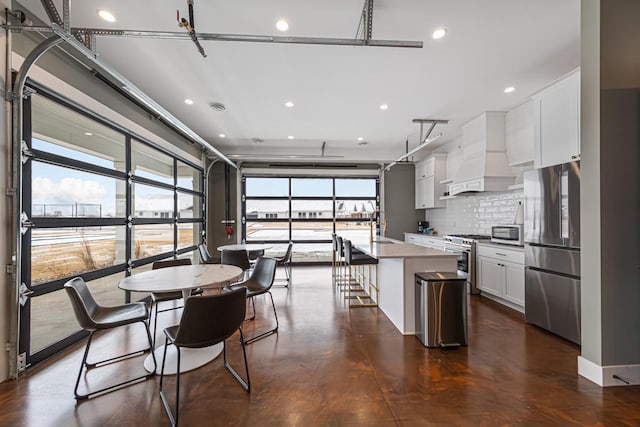 kitchen with premium range hood, appliances with stainless steel finishes, tasteful backsplash, white cabinetry, and a center island with sink