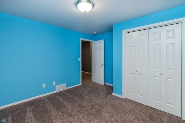 unfurnished bedroom with baseboards, visible vents, dark carpet, and a closet