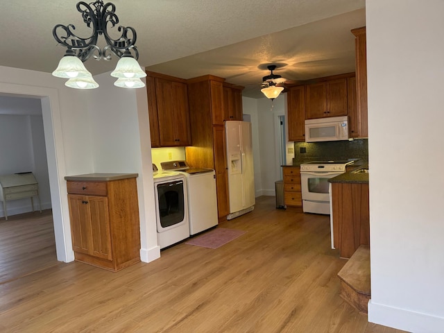 kitchen with hanging light fixtures, light hardwood / wood-style flooring, white appliances, independent washer and dryer, and tasteful backsplash