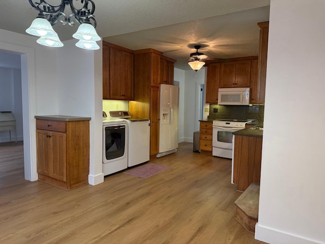 kitchen with white appliances, washer and clothes dryer, decorative light fixtures, decorative backsplash, and light wood-type flooring