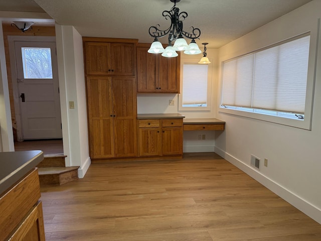 kitchen featuring light wood-type flooring, a notable chandelier, a textured ceiling, built in desk, and pendant lighting