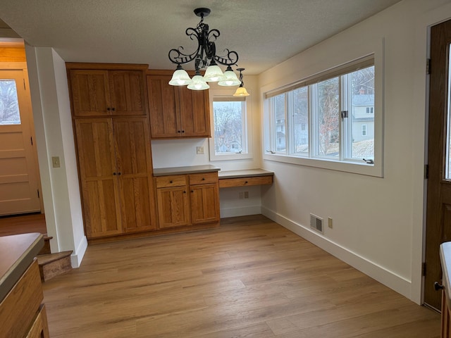 unfurnished dining area featuring an inviting chandelier, pendant lighting, a textured ceiling, light hardwood / wood-style floors, and built in desk