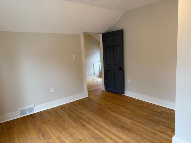 spare room with hardwood / wood-style floors, lofted ceiling, and a textured ceiling