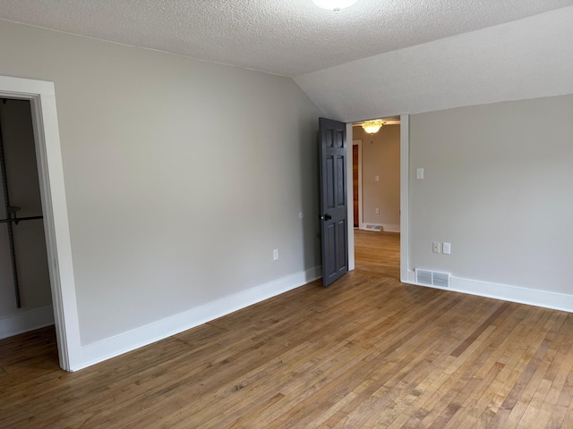 unfurnished room with wood-type flooring, a textured ceiling, and lofted ceiling