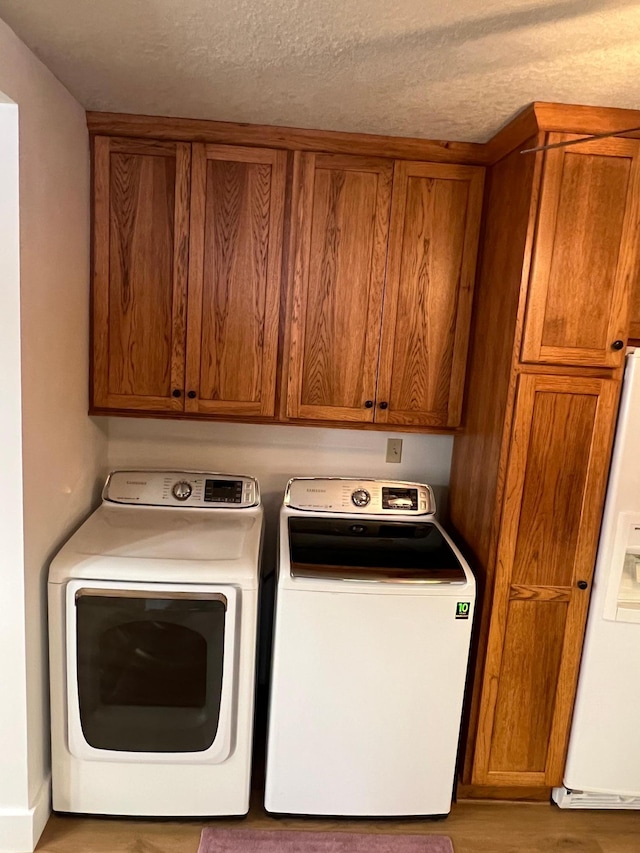 laundry room featuring washer and dryer, cabinets, a textured ceiling, and light hardwood / wood-style flooring