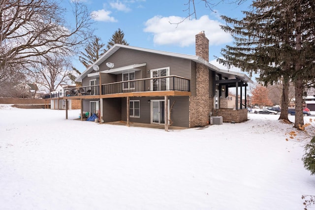 snow covered property with a wooden deck, central AC unit, and a chimney