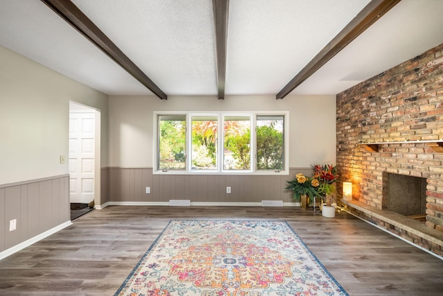 unfurnished living room featuring wood-type flooring, beam ceiling, a brick fireplace, and a textured ceiling