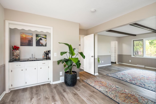 interior space featuring sink, beam ceiling, white cabinets, and light wood-type flooring