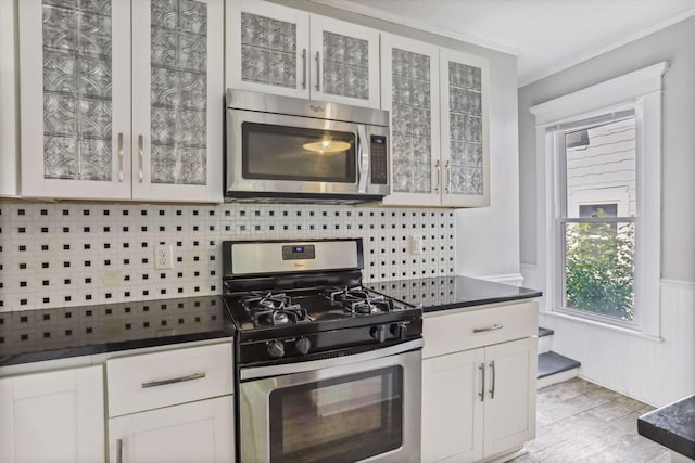 kitchen featuring appliances with stainless steel finishes, tasteful backsplash, white cabinets, light hardwood / wood-style floors, and crown molding