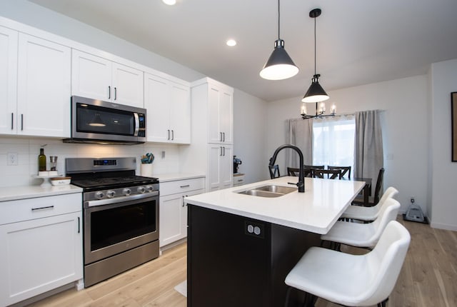 kitchen with white cabinetry, sink, hanging light fixtures, a kitchen island with sink, and stainless steel appliances