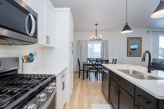 kitchen featuring pendant lighting, white cabinetry, sink, light hardwood / wood-style floors, and stainless steel appliances