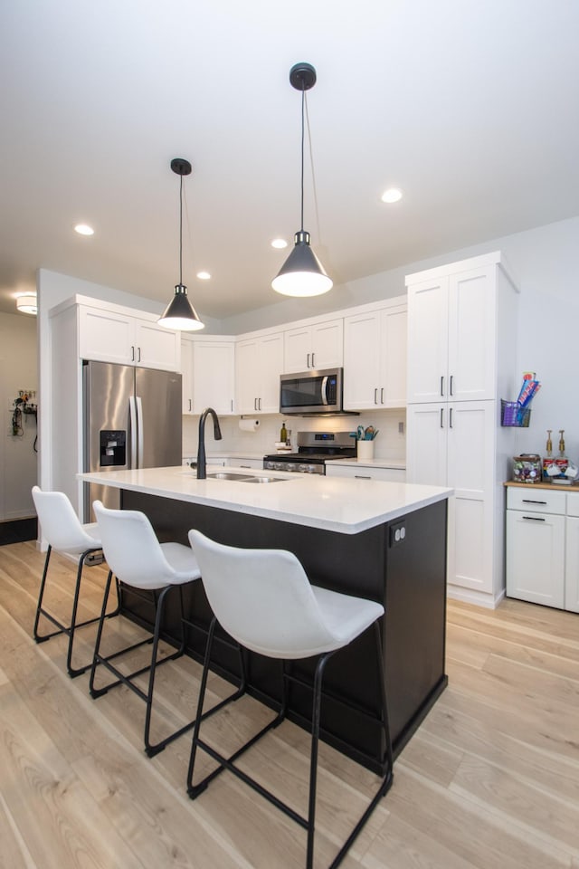 kitchen with sink, white cabinetry, a kitchen island with sink, stainless steel appliances, and decorative light fixtures