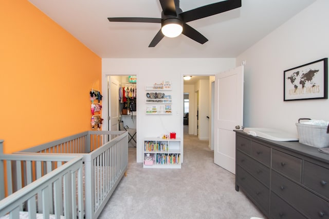 bedroom with a walk in closet, light carpet, a closet, a nursery area, and ceiling fan