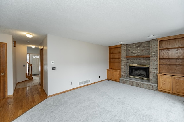 unfurnished living room featuring light carpet, built in shelves, a fireplace, and a textured ceiling