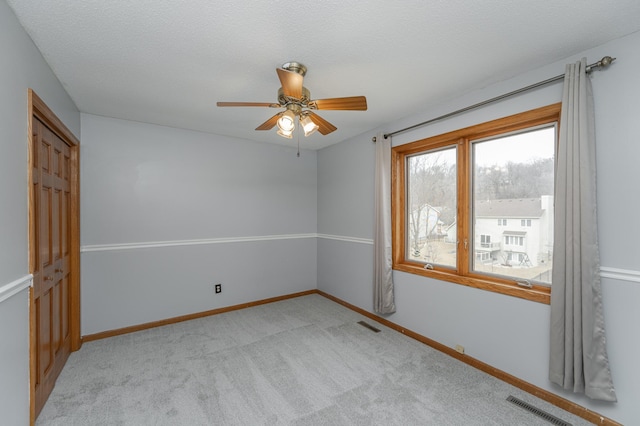 spare room featuring ceiling fan, light colored carpet, and a textured ceiling