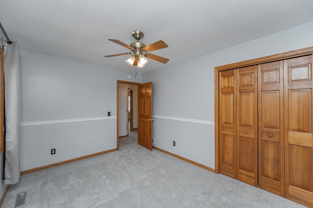 unfurnished bedroom with ceiling fan, light carpet, a textured ceiling, and a closet