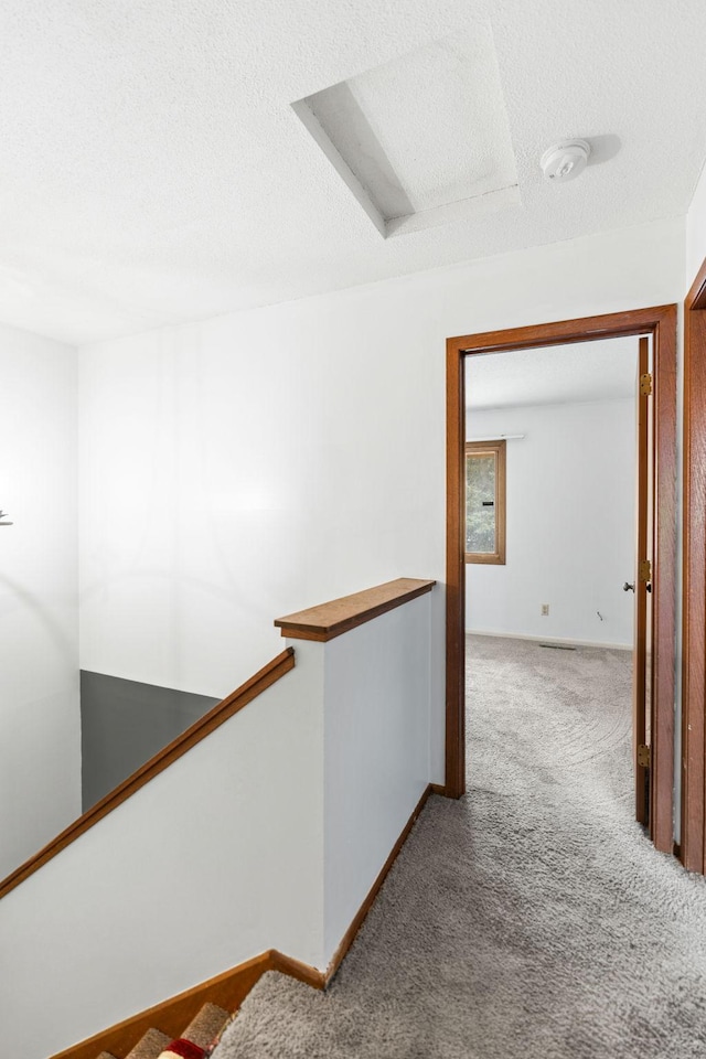 hallway with light colored carpet and a textured ceiling