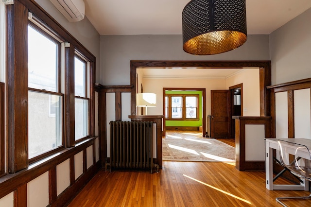 foyer with an AC wall unit, wood finished floors, and radiator