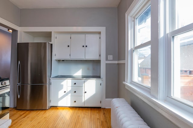 kitchen featuring stainless steel countertops, white cabinetry, light wood-type flooring, freestanding refrigerator, and radiator